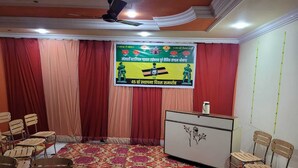 A conference room with a patterned carpet, a podium, and chairs arranged around a table. - New Samrat Hotel And Restaurant (Srinagar)