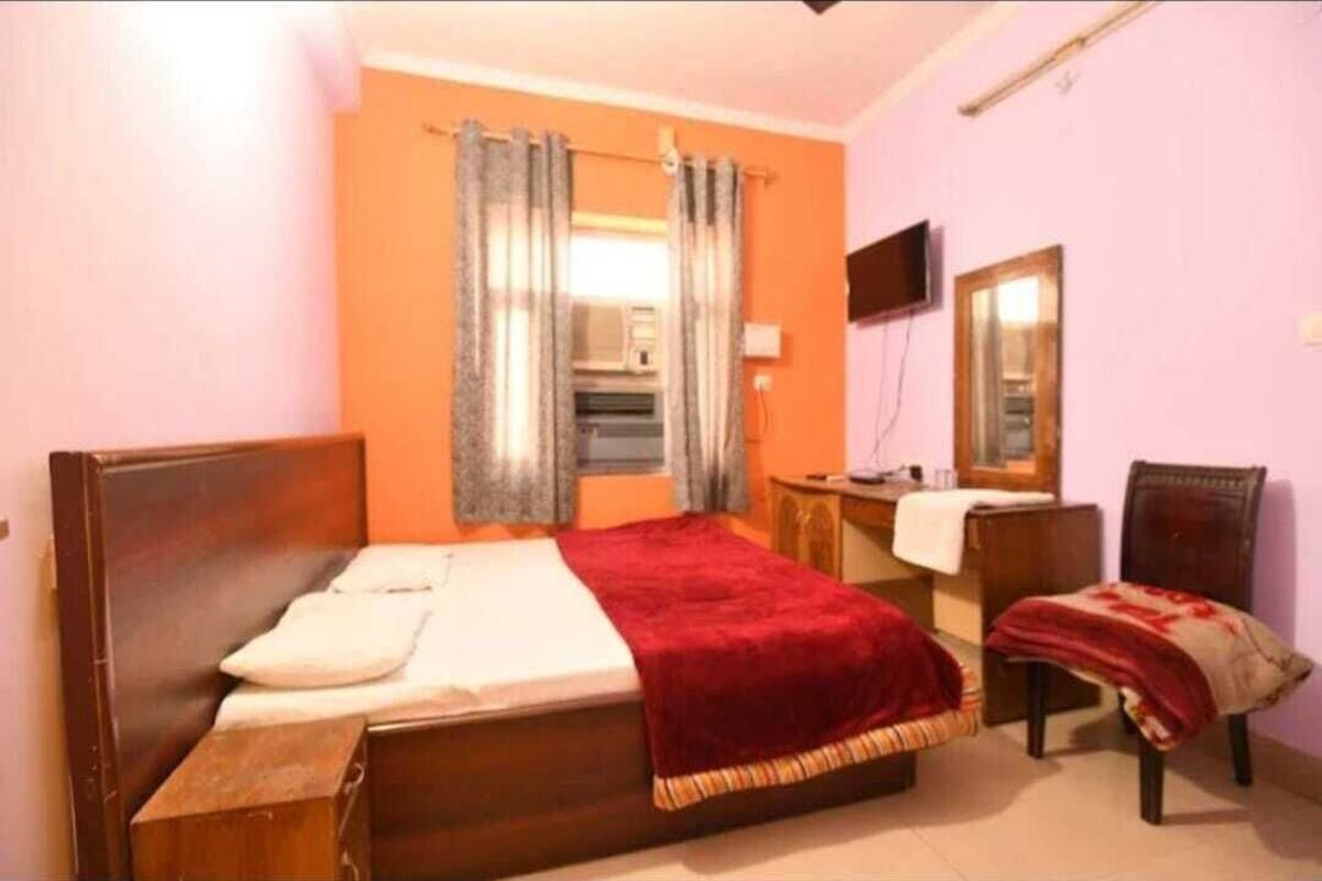 A bedroom with a single bed, a wooden nightstand, a desk, a chair, a television, and a mirror.