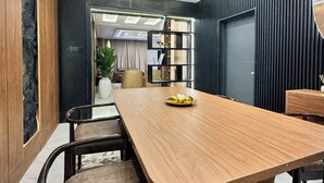 A modern dining area with a wooden table and chairs, a built-in bookshelf, and a decorative mirror on the wall. - Lumora Apartments (Abuja)