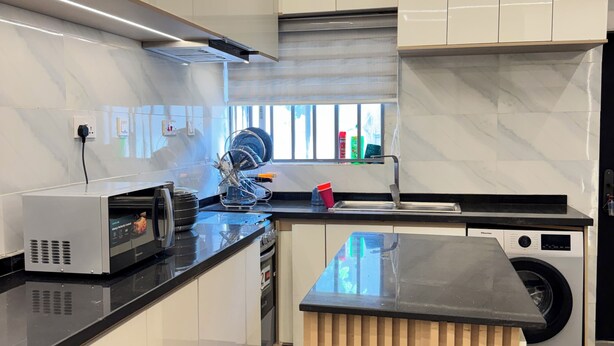 A modern kitchen with a built-in microwave, oven, and washing machine. - Lumora Apartments (Abuja)