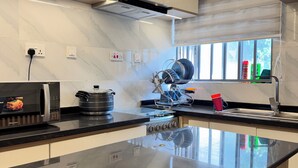 A modern kitchen with a black countertop, stainless steel appliances, and a dish rack. - Lumora Apartments (Abuja)