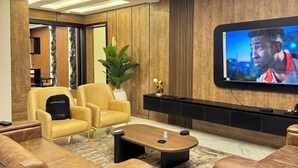 A modern living room with a flat-screen TV mounted on the wall, leather sofas, a coffee table, and a decorative plant. - Lumora Apartments (Abuja)