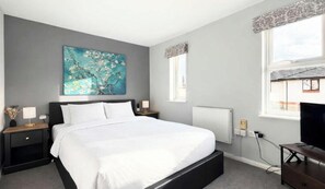 A bedroom with a large bed, a nightstand, a wall-mounted TV, and a window with a view.