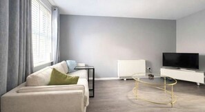 A modern living room with a sofa, a glass coffee table, a TV, and a radiator.