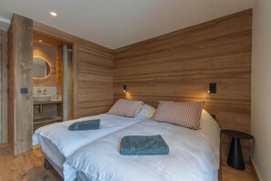 A bedroom with two beds, wooden walls, a round mirror, a sink, and a small table. - Chalet Combloux, Megève, Mont-Blanc View (Combloux)