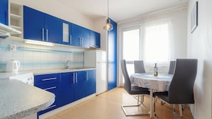 A modern kitchen with blue cabinets, a white refrigerator, and a dining area with a table and chairs. - Perfect for Teams & Families: 3-Bedroom Flat, 7 Guests, Balcony, Close to Centre (Bratislava)