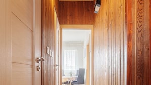 A wooden-paneled hallway with a door on the left and a dining area in the background. - Perfect for Teams & Families: 3-Bedroom Flat, 7 Guests, Balcony, Close to Centre (Bratislava)