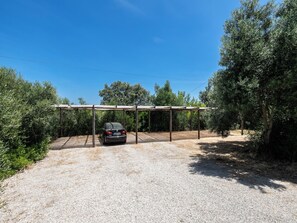 A gravel driveway leading to a covered parking area with a car parked under a wooden structure. - Olea Green Studio 1, Tavira, Algarve (Querença)