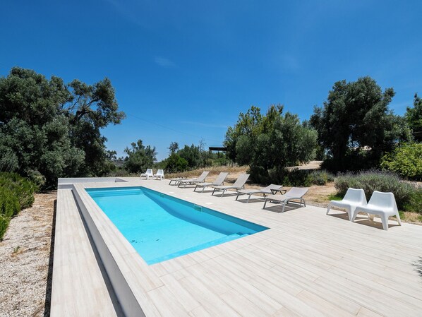 A rectangular swimming pool with a wooden deck, surrounded by white lounge chairs and greenery. - Olea Green Studio 1, Tavira, Algarve (Querença)