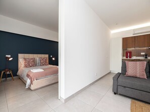 A modern bedroom with a bed, bedside lamps, and a nightstand. Adjacent to the bedroom is a kitchenette with a countertop and cabinets. - Olea Green Studio 1, Tavira, Algarve (Querença)