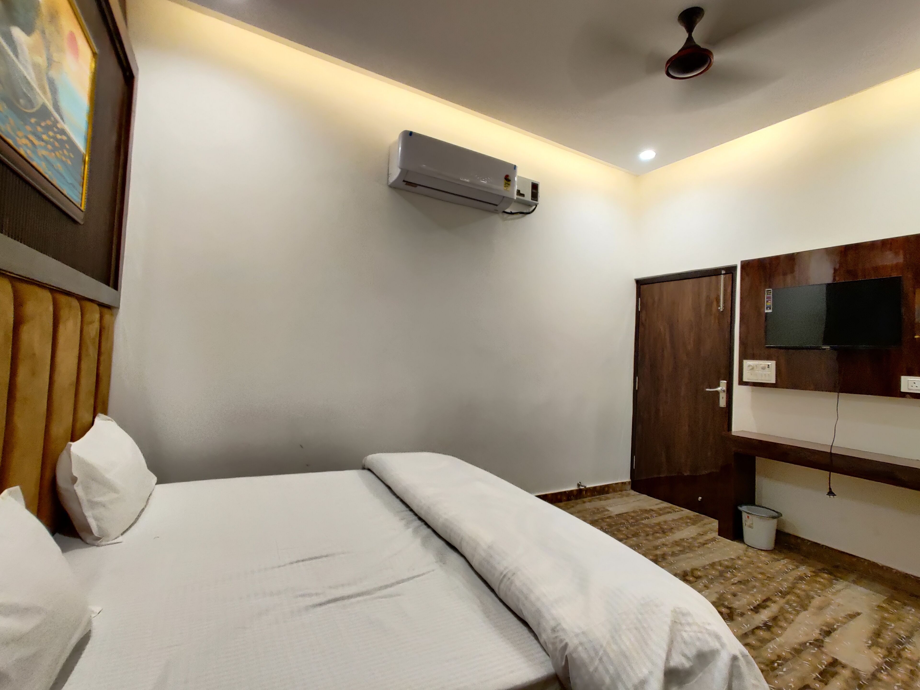 Habitación de hotel con cama, aire acondicionado, televisor montado en la pared y ventilador de techo.