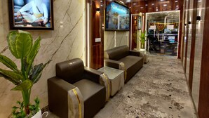 A lobby with marble walls, a ceiling fan, and seating areas. - Taj Pride Inn (Amritsar)