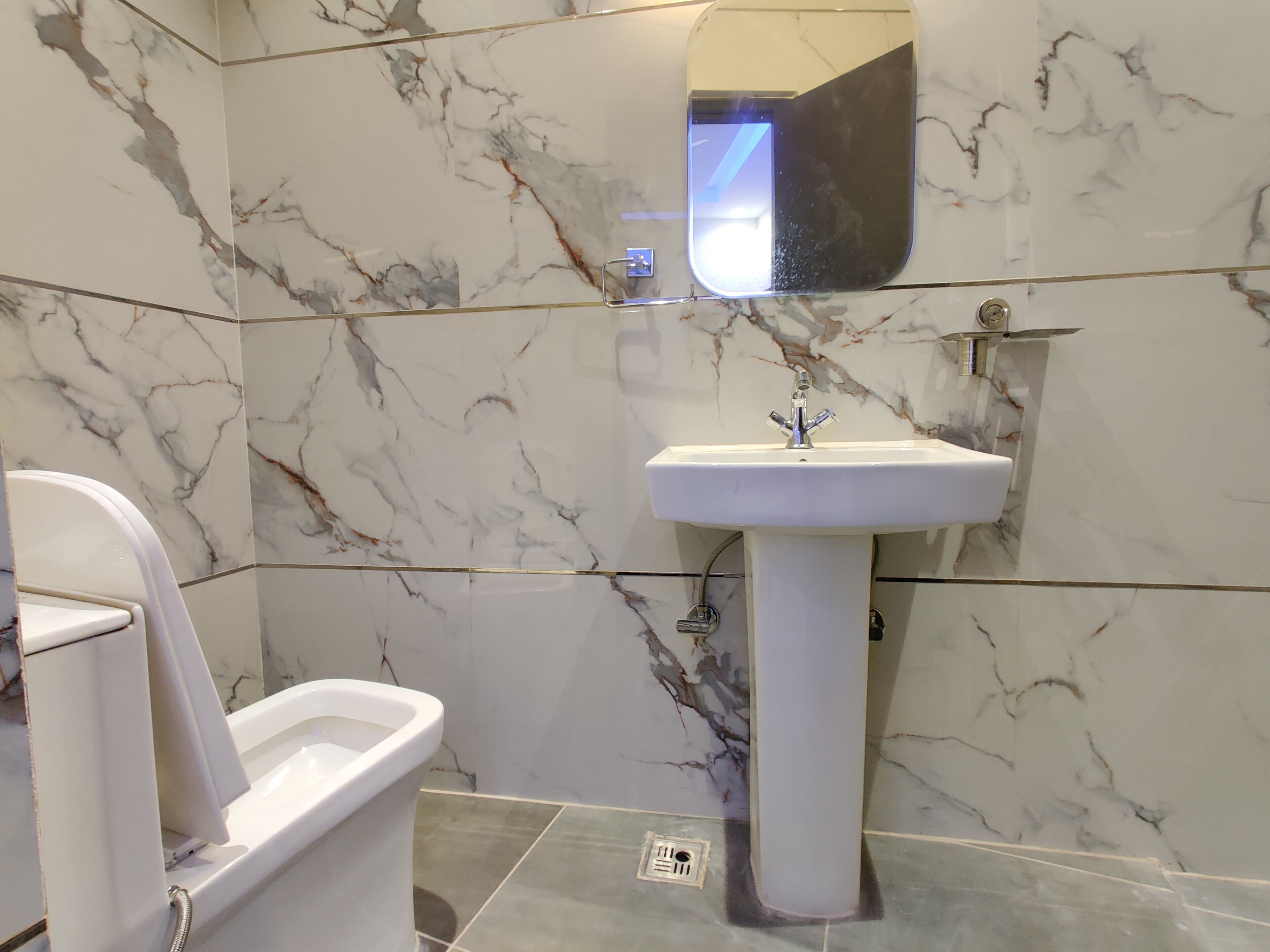 A bathroom with a toilet, sink, and marble walls.