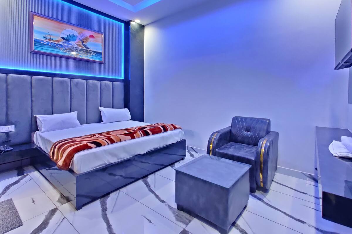 A modern bedroom with a bed, a chair, a small table, and a painting on the wall.