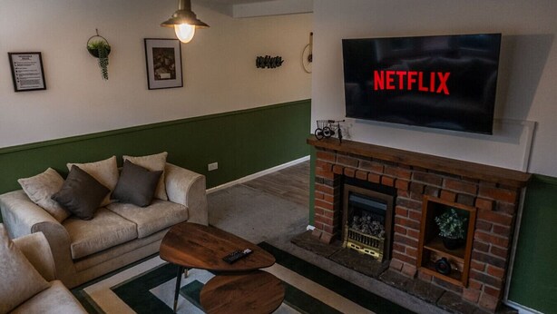 Olohuone, jossa on yksi seinä maalattu vihreällä korostevärillä, takka, sohva ja televisio, jossa näkyy teksti ”NETFLIX”.