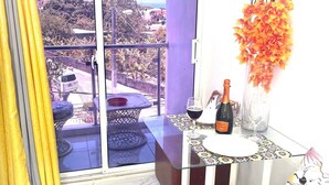 A balcony with a view of a cityscape, a table with a bottle of wine, a glass, and a vase with flowers. - Room-royal Terrace Queen 1 (Puerto Plata)