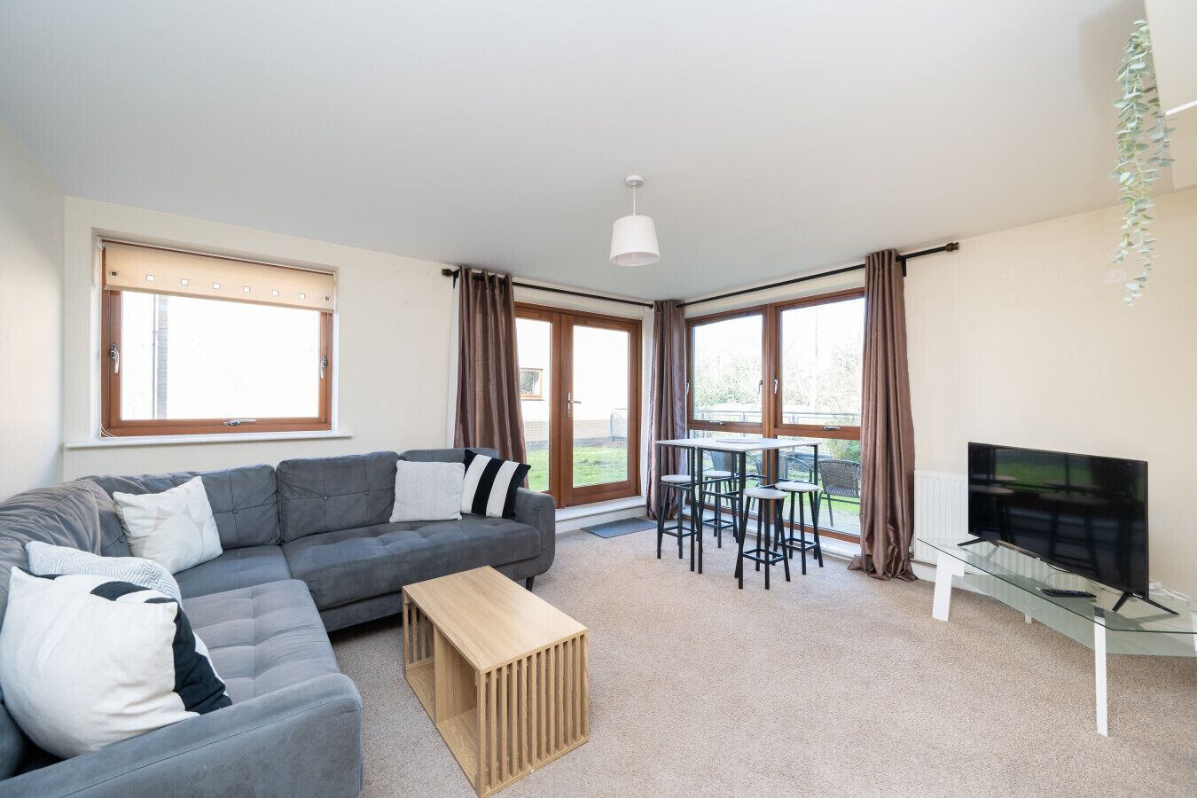 A modern living room with a grey sofa, a wooden coffee table, a glass TV stand, and a dining area with a table and chairs.