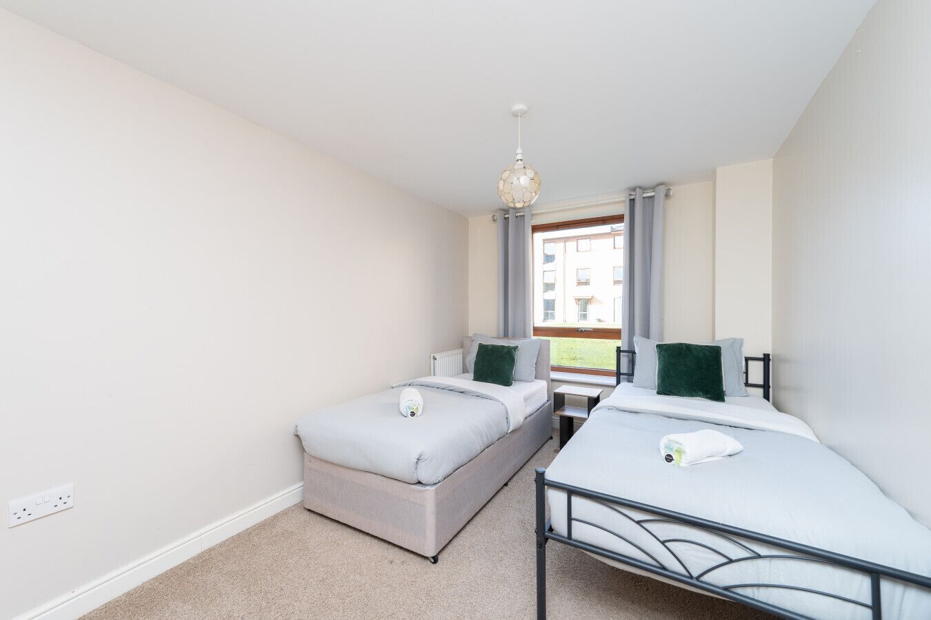 A bedroom with two single beds, a small table, and a window with curtains.
