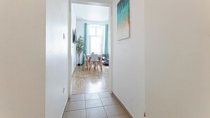 A hallway leading to a dining area with a table and chairs, a potted plant, and a painting on the wall. - Elegant Spacious 2BR City Center Stay (Vienna)