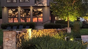 Une maison moderne à deux étages, dotée de grandes fenêtres, d’un mur en pierre et d’un jardin bien entretenu.