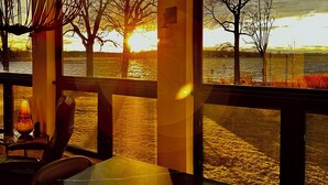 Un espace repas offrant une vue sur un coucher de soleil se reflétant sur une étendue d’eau, une table avec des chaises et un luminaire suspendu.