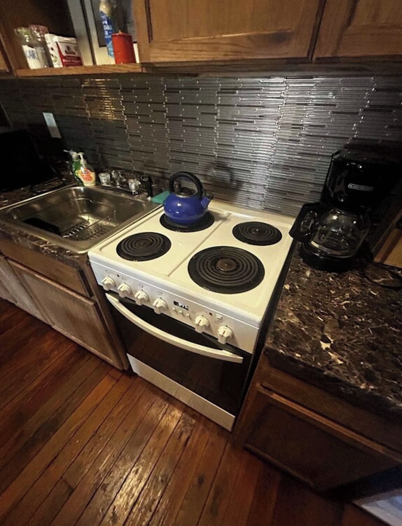 A kitchen with a white stove, a blue kettle, a coffee maker, and wooden cabinets.