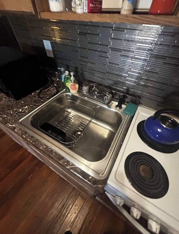 Una cocina con un lavamanos de acero inoxidable, una estufa con una perilla azul y un respingo de azulejos.
