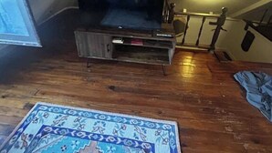 Un petit dormitori a l'àtic amb un televisor sobre un suport de fusta, una catifa amb dibuixos i una escala que condueix al pis superior.