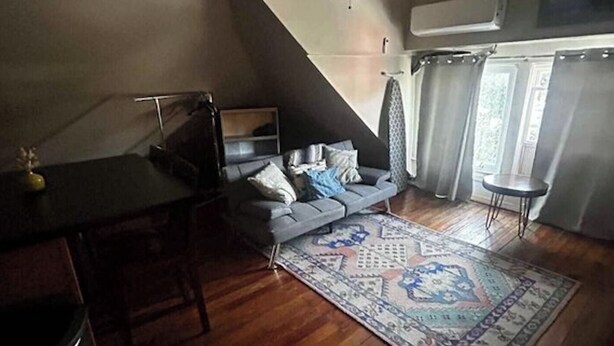 Un dormitori d'estil loft amb sostre inclinat, un sofà gris, una catifes amb dibuixos i una taula petita.