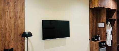 Una habitación de hotel moderna con una televisión de pantalla plana en la pared, un escritorio con lámpara, un mini refrigerador y una bata colgada en un perchero.