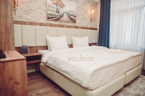 A neatly made bed with white linens and towels, a wooden nightstand with a lamp, and a painting above the bed. - SM Luxury Hotel (Fergana)