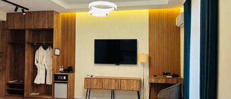 Una habitación de hotel moderna con un armario de madera, un televisor montado en la pared, un escritorio con una silla, una mesa de centro redonda y un sofá azul.