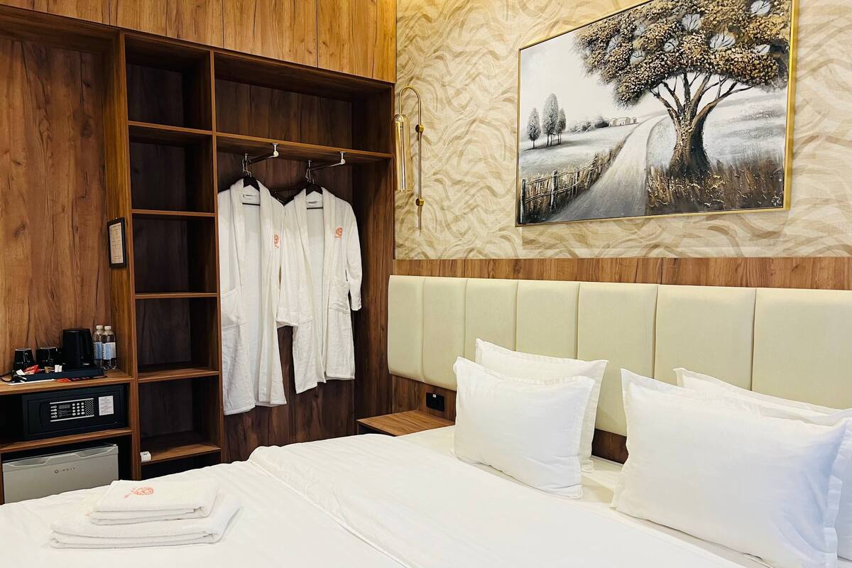 Een hotelkamer met een bed, een houten garderobe en een schilderij van een boom aan de muur.