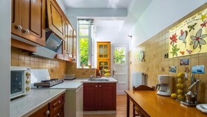 A kitchen with wooden cabinets, a built-in oven, a coffee maker, and a window with a view of greenery. - Spacious & Modern Retreat with Sun Terrace in Neos Kosmos, Athens (Athina)