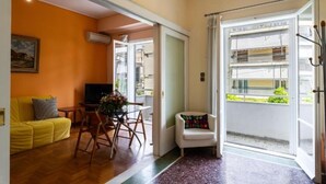 A living room with a yellow sofa, a dining table with chairs, a TV, and a balcony with a railing. - Spacious & Modern Retreat with Sun Terrace in Neos Kosmos, Athens (Athina)