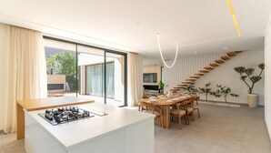 A modern kitchen with a central island, a dining area with a wooden table and chairs, and a staircase with wooden steps. - Villa Hamza with private pool - My Rental Homes (Oulad Ikhia)