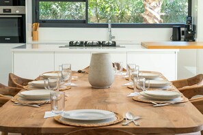 A dining table set for six with plates, glasses, and cutlery, a large vase centerpiece, and a window with a view of greenery. - Villa Hamza with private pool - My Rental Homes (Oulad Ikhia)