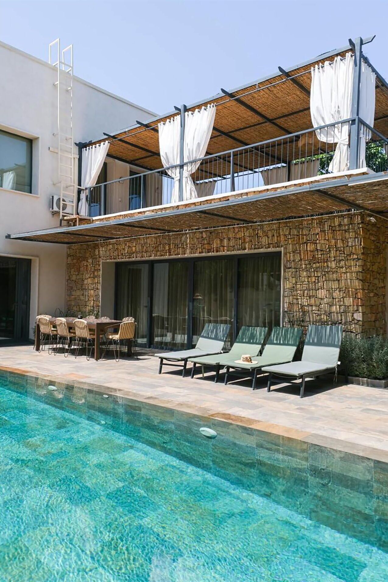Une villa moderne dotée d’une piscine, d’un espace salon extérieur et d’une façade en pierre.