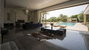 Ein modernes Wohnzimmer mit einem großen Glasfenster zum Poolbereich, einem Kamin und einem Ledersofa.