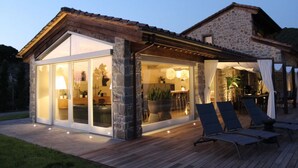 Una casa moderna con fachada de piedra y grandes puertas de cristal que dan a un patio con mobiliario exterior.