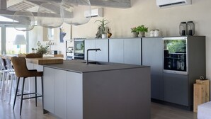 Una cocina moderna con una isla central, taburetes de bar, luces colgantes y un refrigerador empotrado.
