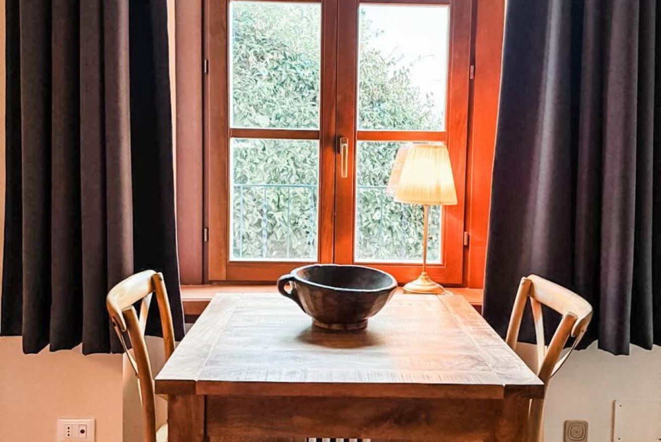 A dining table with a bowl, chairs, a window with curtains, and a lamp.