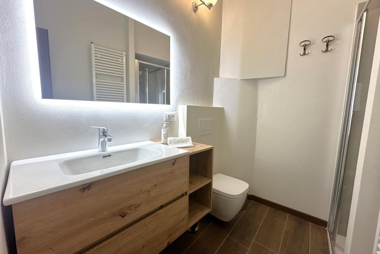 A bathroom with a white sink, wooden vanity, a white toilet, and a shower area.