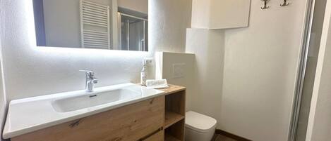 A bathroom with a white sink, wooden vanity, a white toilet, and a shower area.