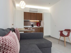 A modern living room with a grey sectional sofa, a small dining table, and a red chair. - Olea Black Studio 2, Tavira, Algarve (Querença)