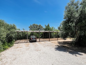 A gravel driveway leading to a covered parking area with a car parked under a wooden structure. - Olea Black Studio 2, Tavira, Algarve (Querença)