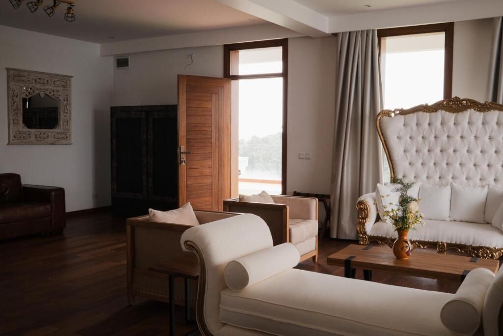 A living room with a large white sofa, a brown leather armchair, and a wooden coffee table with a vase of flowers.