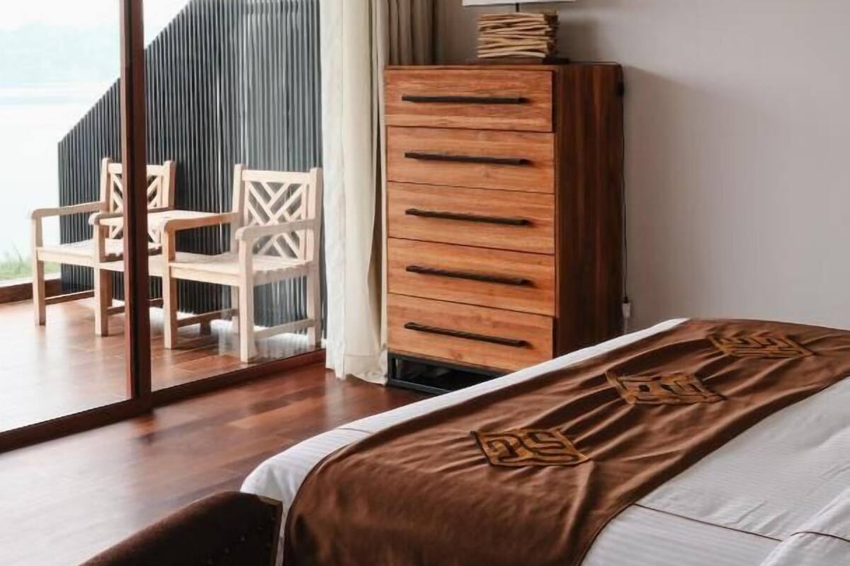 Une chambre d’hôtel avec un lit, une commode en bois, une chaise et une vue sur l’extérieur.