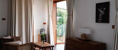 Una habitación con sofá de madera, una mesita con un florero, un mueble de madera y un ventanal con cortinas.