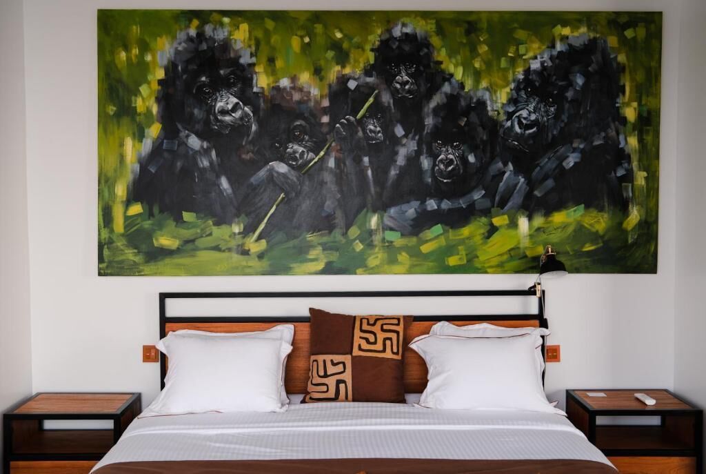 A hotel room with a large abstract painting of gorillas on the wall, a wooden headboard, two white pillows, and a brown patterned pillow.